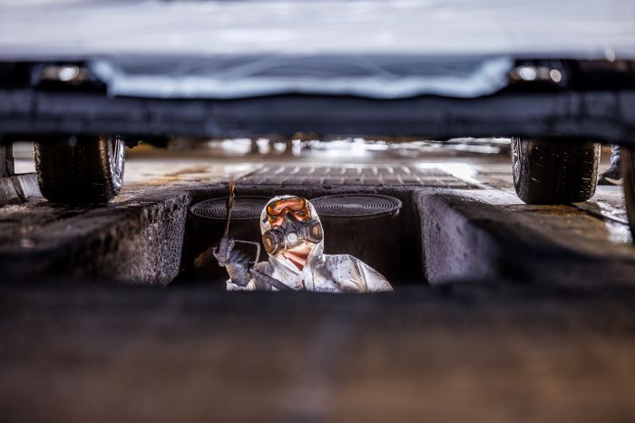 Amports worker performing an undercoating of a car, wearing a full protective suit and mask