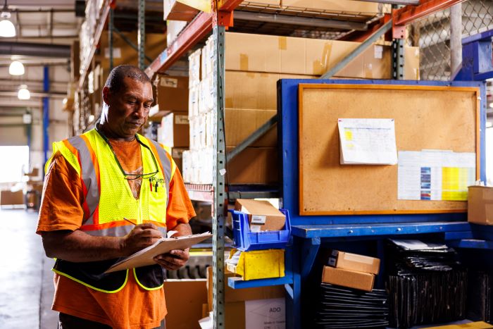 Amports staff writing on papers attached to a clipboard at a warehouse