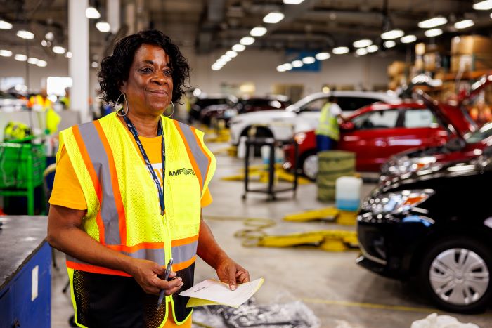 Amports worker holding a pen and paper at a busy auto garage workshop