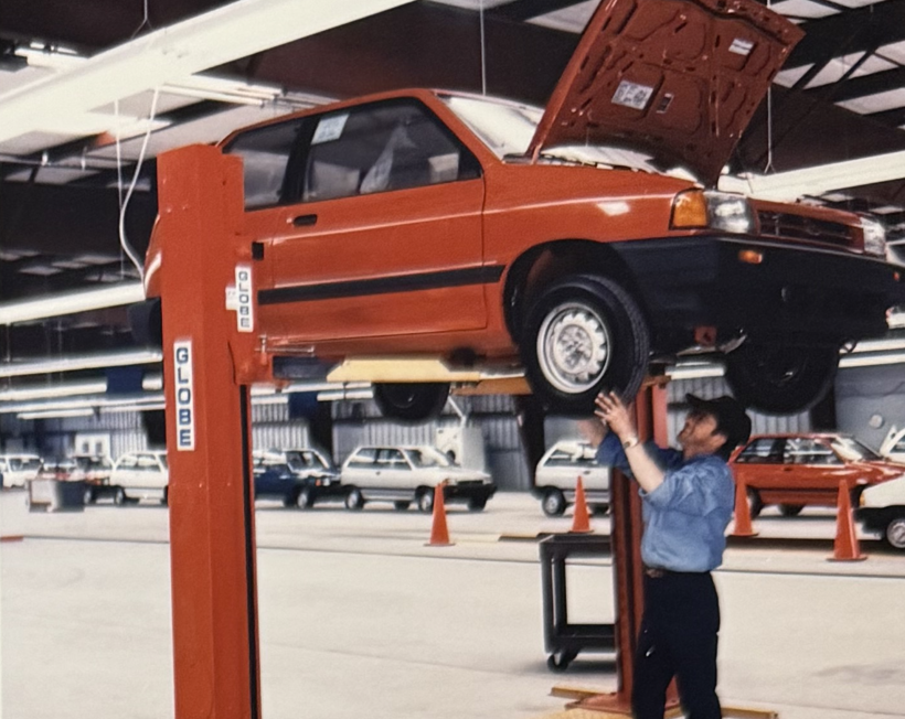 A vintage photograph of an Amports' mechanic working below a lifted red car