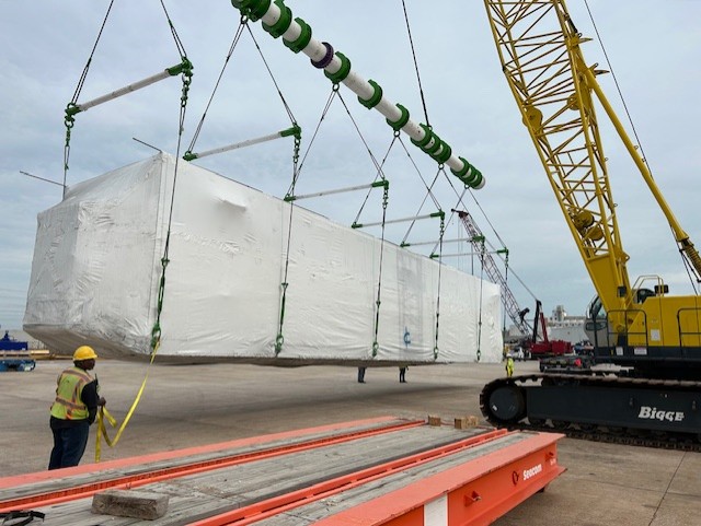 A yellow crane arm carrying a white-wrapped cargo container