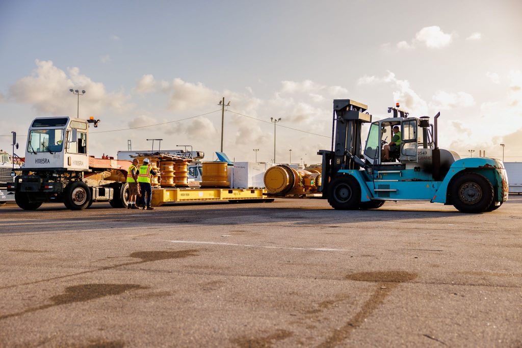 Ground-level view of Amports port workers using a white truck and a blue forklift to handle heavy cargo