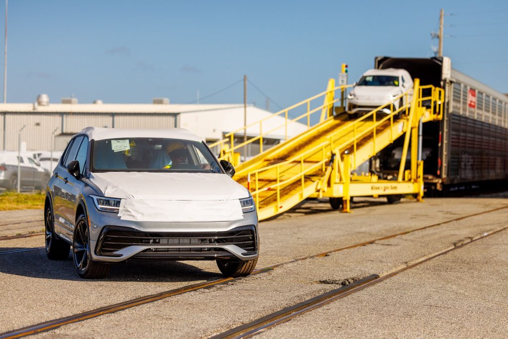 Amports workers drive two SUVs off the auto racks using yellow portable ramps.