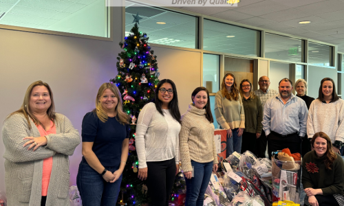 A group portrait of Amports team near a Christmas tree and wrapped gifts