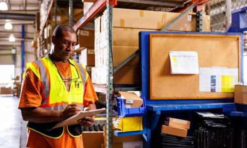 Amports staff writing on papers attached to a clipboard at a warehouse