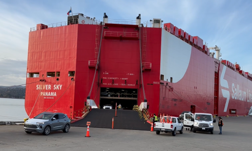 A photo of red RoRo ship unloading vehicles with a ramp
