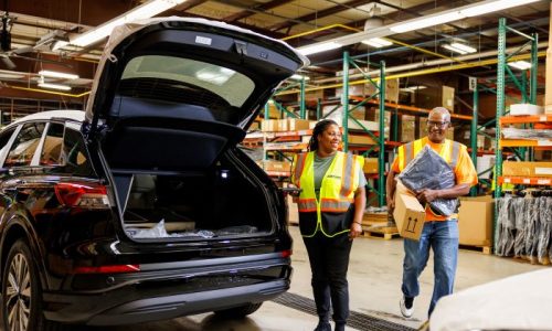 Two Amports workers having a conversation near an open SUV trunk at a warehouse